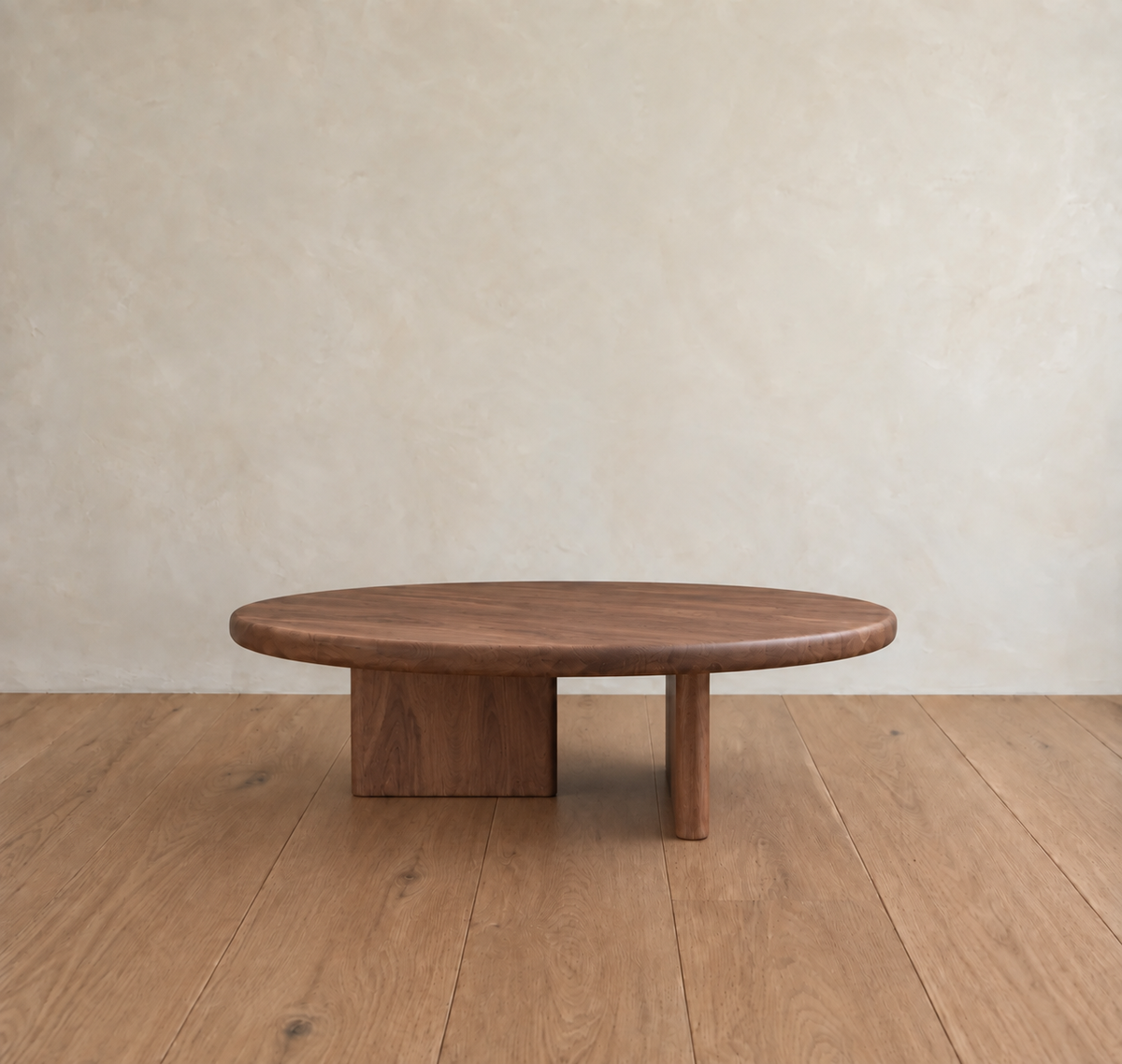 A round coffee table in walnut featuring asymmetrical legs sits on a light wood floor, set against a beige textured wall.