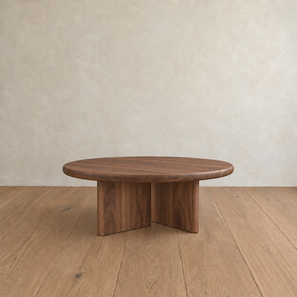 A Round coffee table in walnut with split-panel legs stands on a light wooden floor against a cream-colored textured wall.