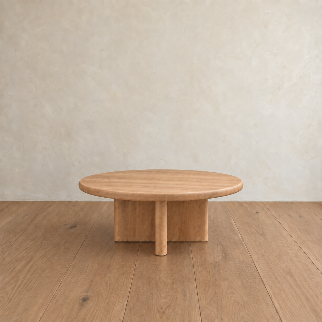 The Round coffee table in white oak, handmade in Vancouver from premium materials, sits on a wooden floor against a beige textured wall, bringing a touch of minimalist elegance to any space.