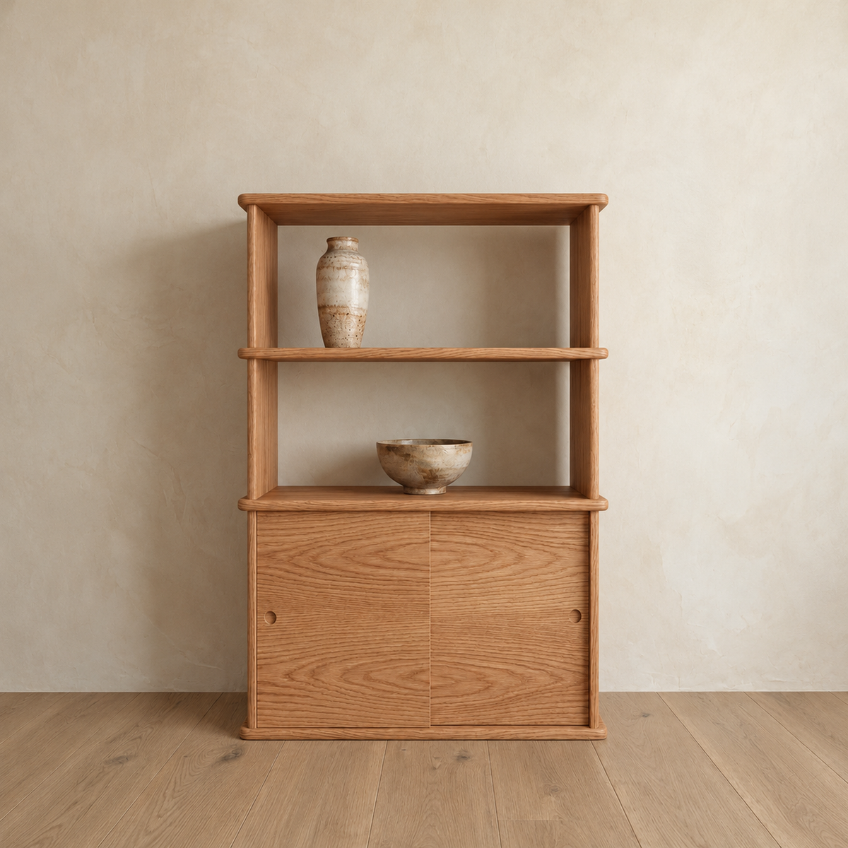 The sliding door bookcase in red oak against a plaster wall, with two open shelves above a sliding-door cabinet, holding a ceramic vase and a bowl.