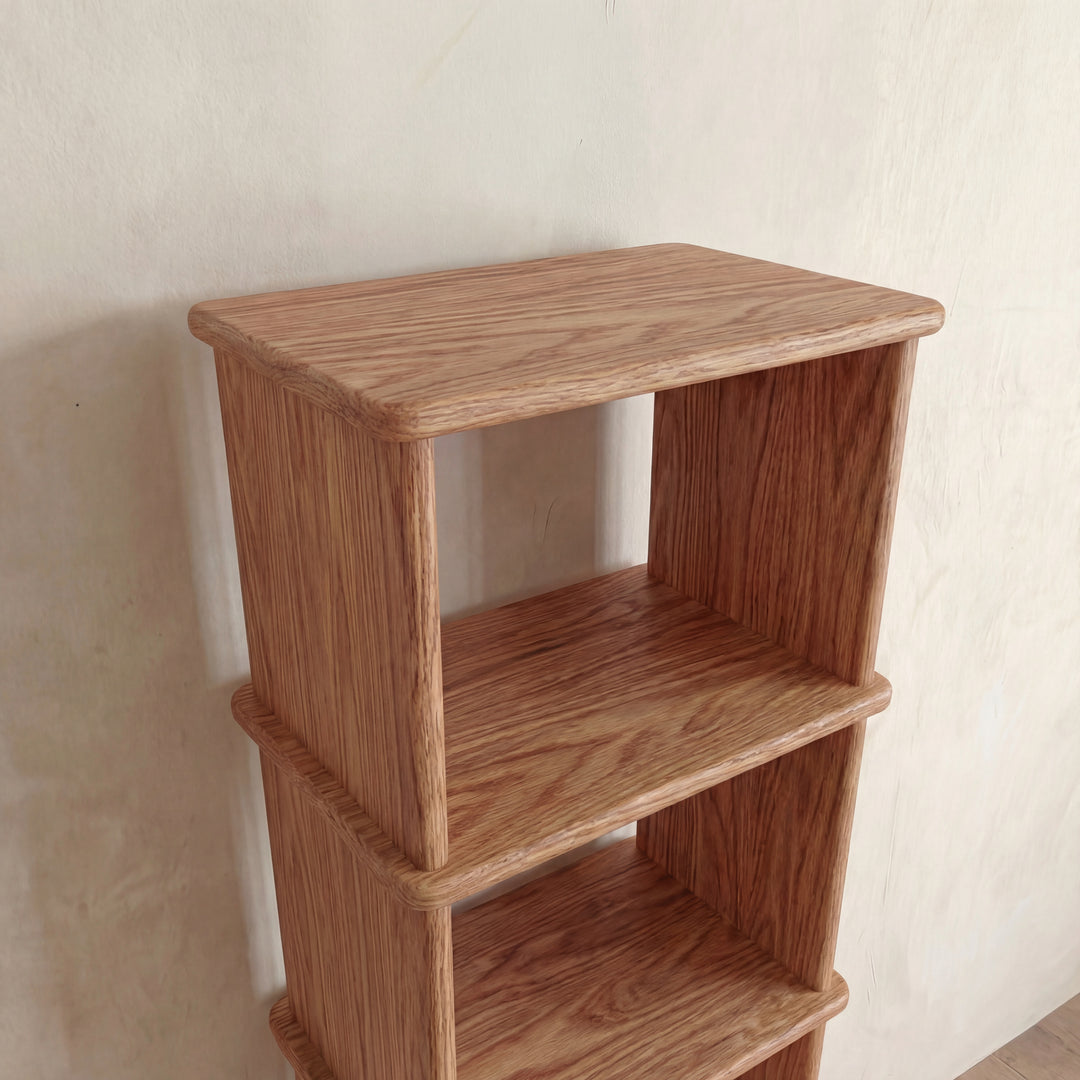 A close-up of the top three shelves of the Narrow bookshelf in red oak, featuring a light natural finish and positioned against a plain, light-colored wall.