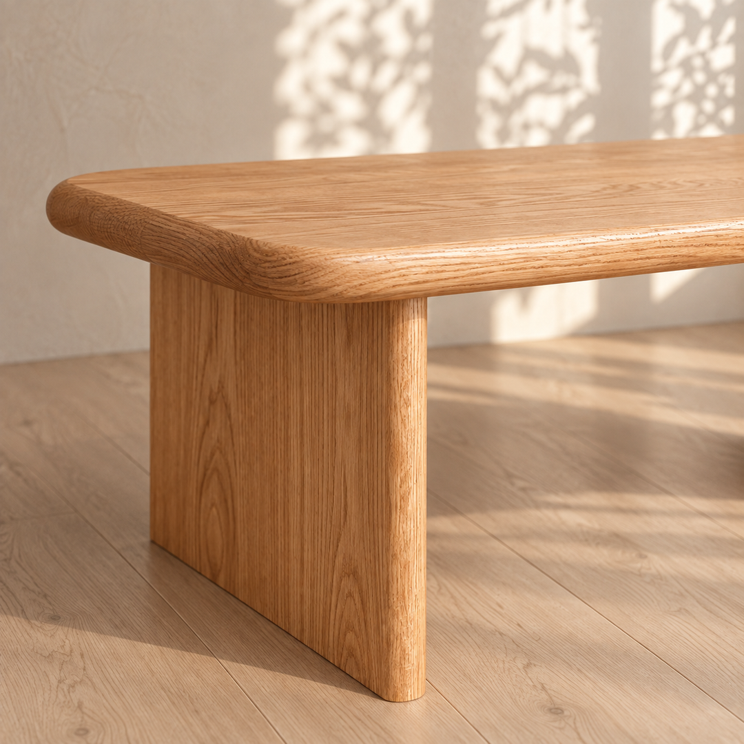 A close-up of the 40 inch coffee table in red oak showcases its handmade construction, rounded edges, and thick legs. Placed on a wooden floor with sunlight and leafy shadows dancing across the wall and surface, this table brings warmth and natural elegance to the room.