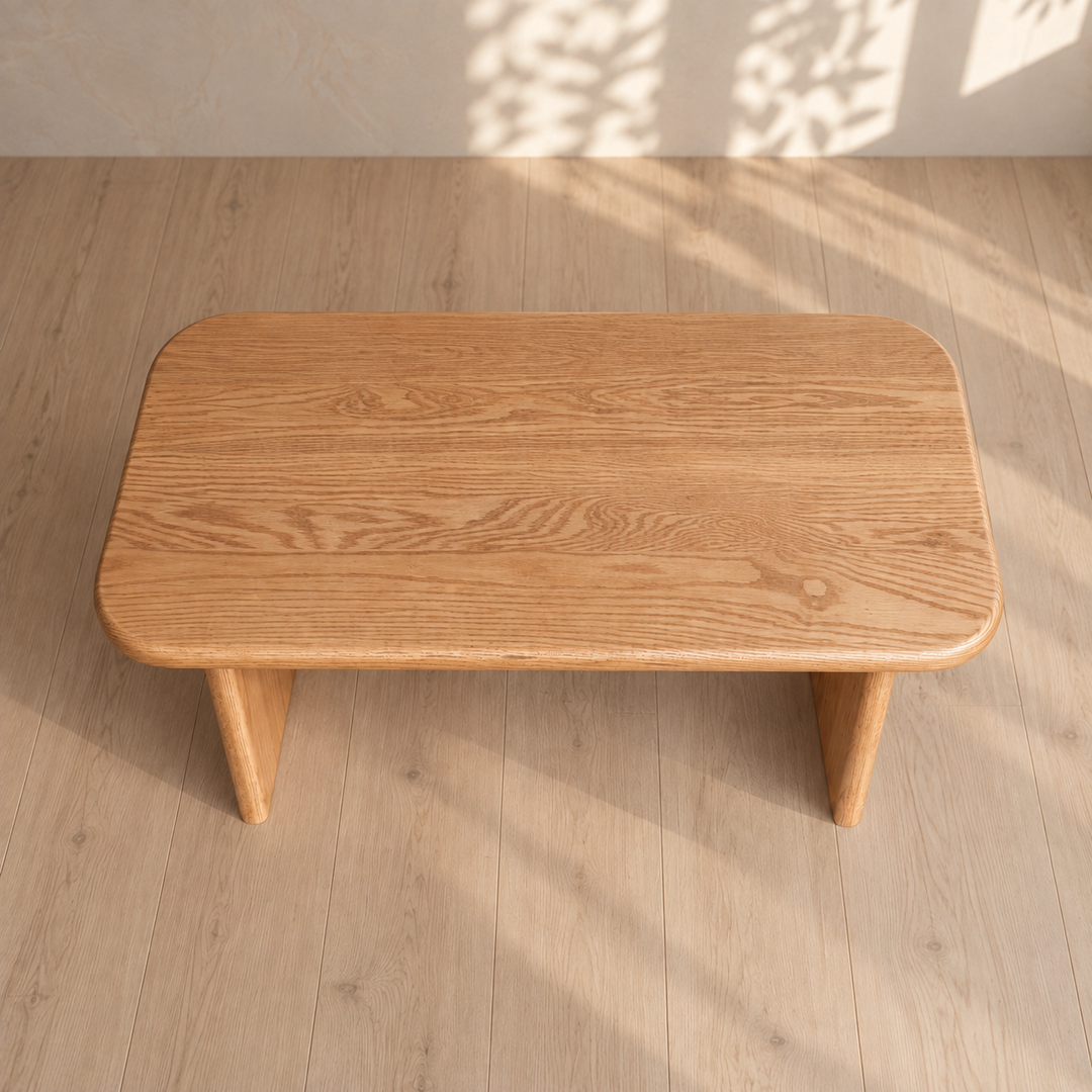 A 40 inch coffee table in red oak, handmade with rounded corners and a rectangular shape, sits on a light wood floor. Bathed in sunlight and leafy shadows, this solid red oak piece creates a warm, natural atmosphere.
