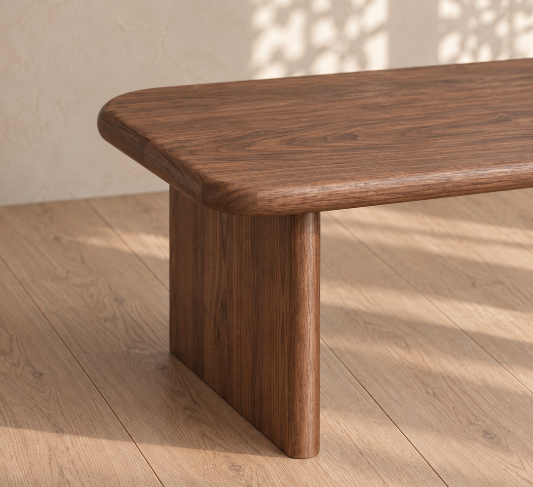 A close-up of the 40 inch coffee table in walnut, featuring smooth, rounded edges and sturdy legs, set on a light wood floor with soft sunlight and leaf shadows in the background.