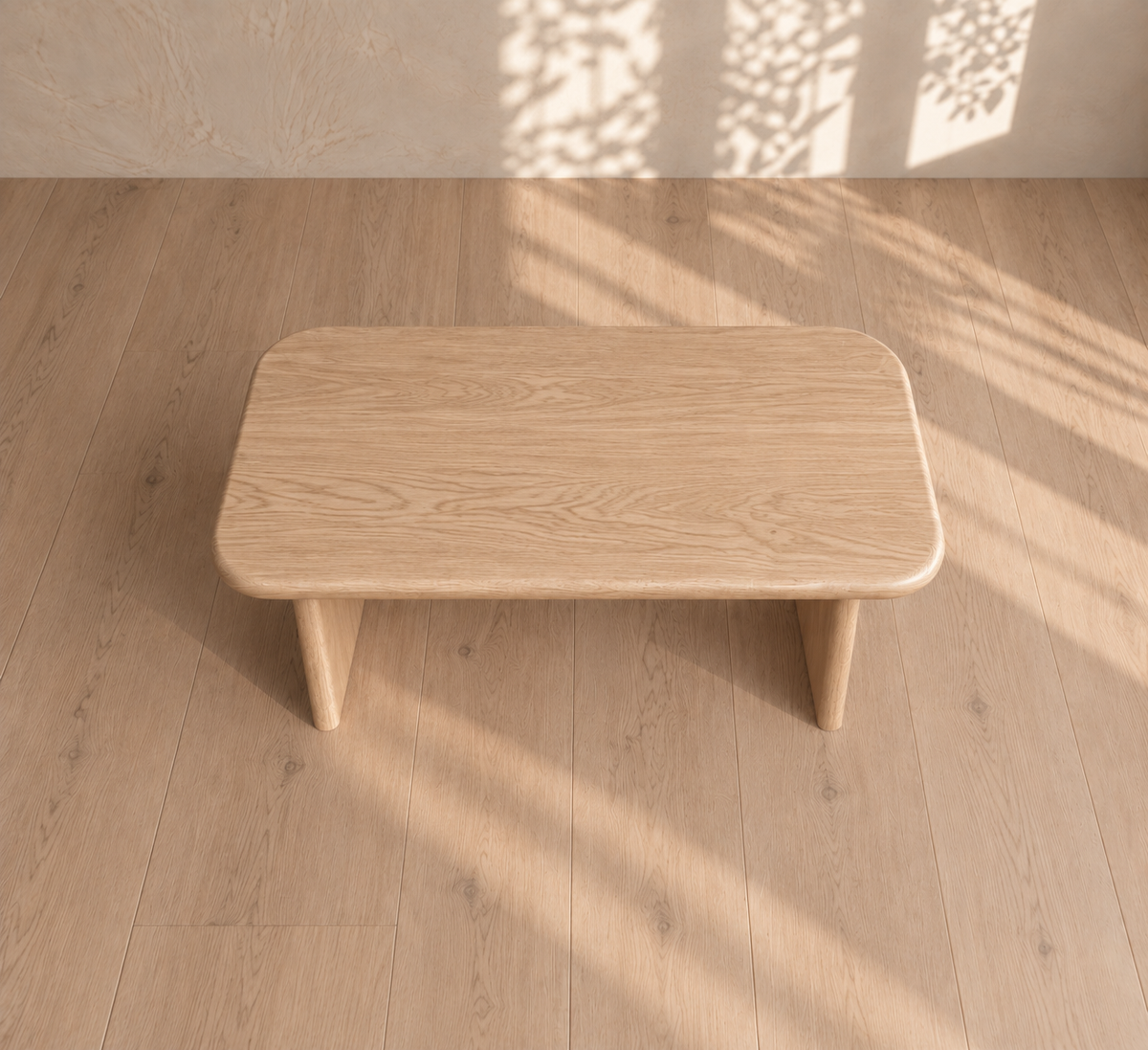The 40 inch coffee table in white oak features a small, rectangular minimalist design with rounded edges, crafted from solid white oak. Resting on a light wood floor and illuminated by soft sunlight with leafy shadows dancing on the wall, this elegant coffee table seamlessly enhances modern interiors with its understated charm.
