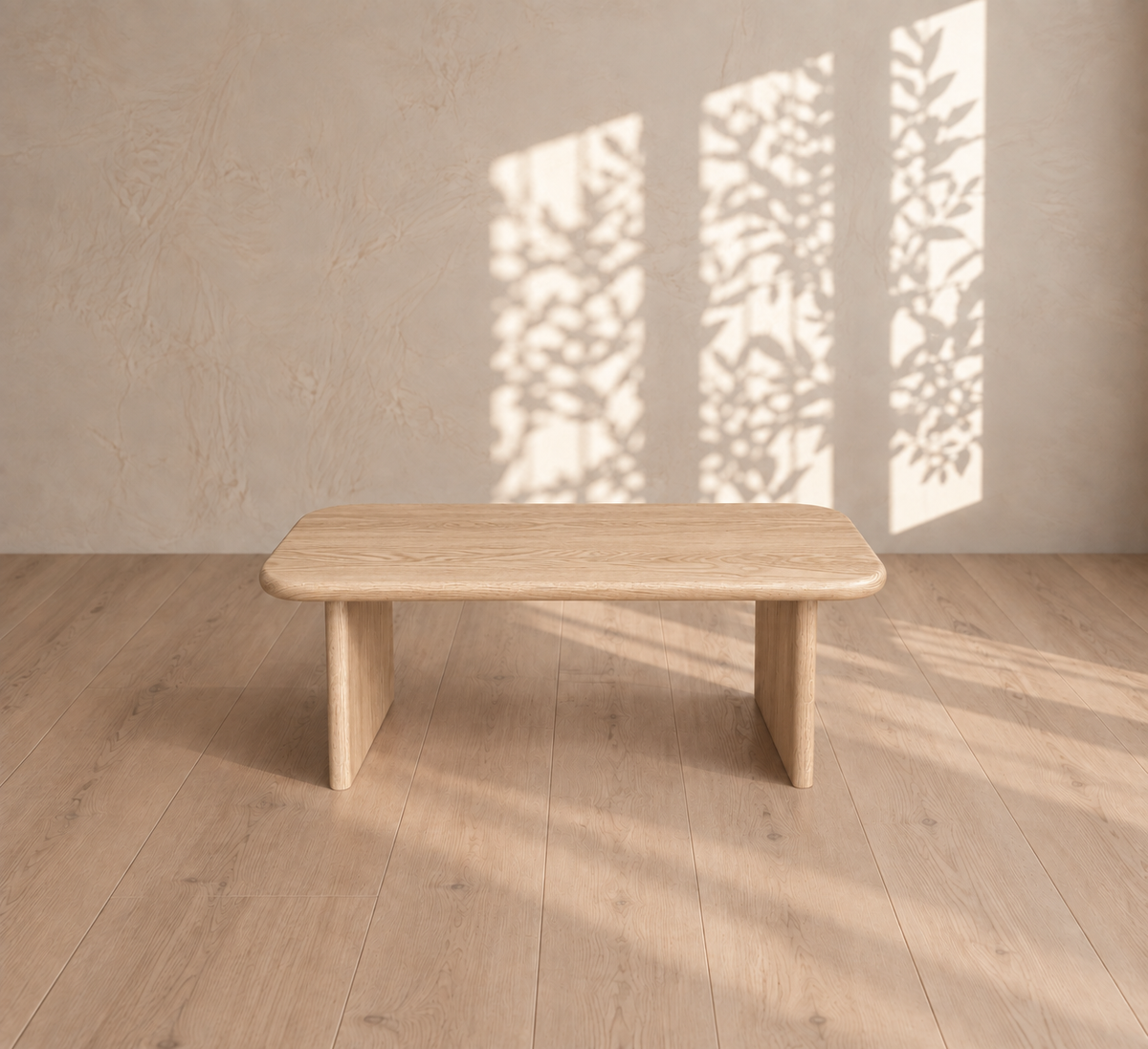 A 40 inch coffee table in white oak sits on a light wood floor. Sunlight filters through a window, casting leafy plant shadows on a beige textured wall behind the table.
