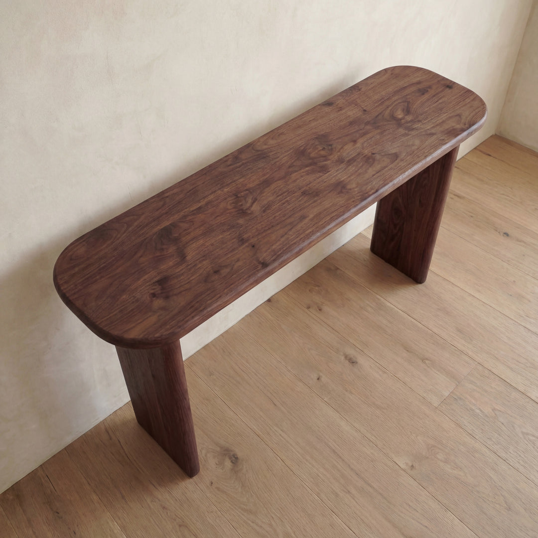 The 60 inch console table in walnut, handmade in Vancouver with rounded edges and a rich brown grain, stands on a light wood floor against a beige wall.