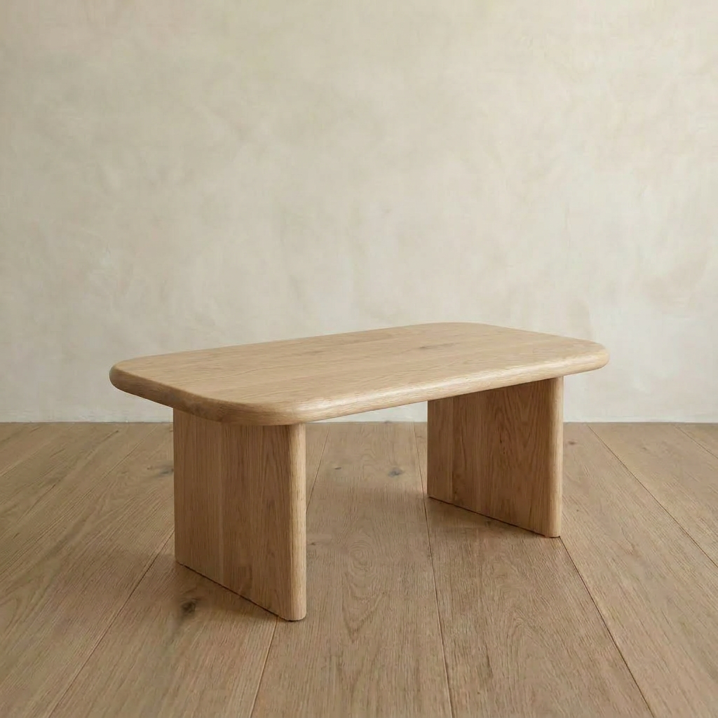 The 40 inch coffee table in white oak features a minimalist design with rounded edges, two wide flat legs, and is shown on a wooden floor against a neutral beige wall.
