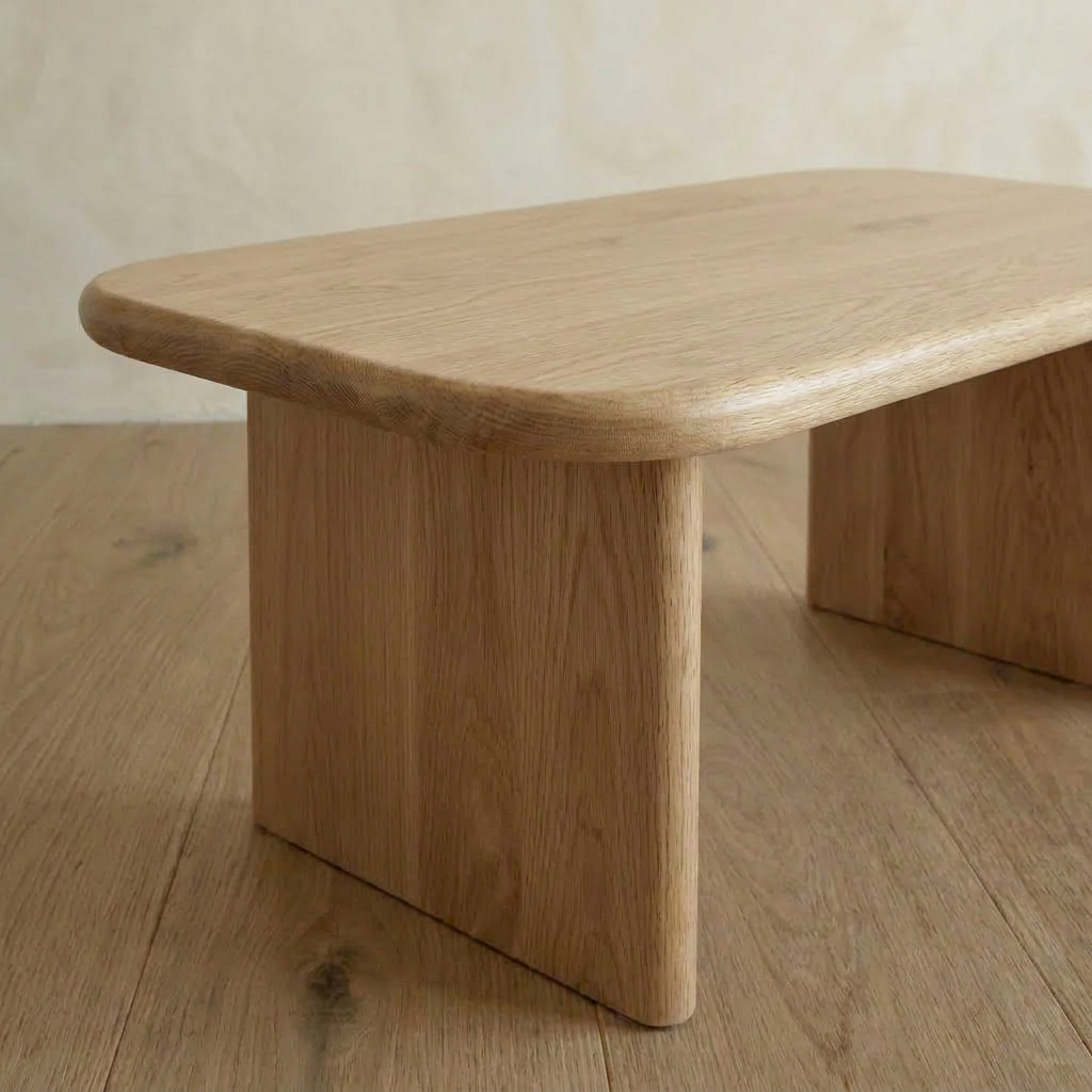 The 40 inch coffee table in white oak features rounded edges and thick, rectangular legs, sitting elegantly on a wooden floor against a light beige wall.
