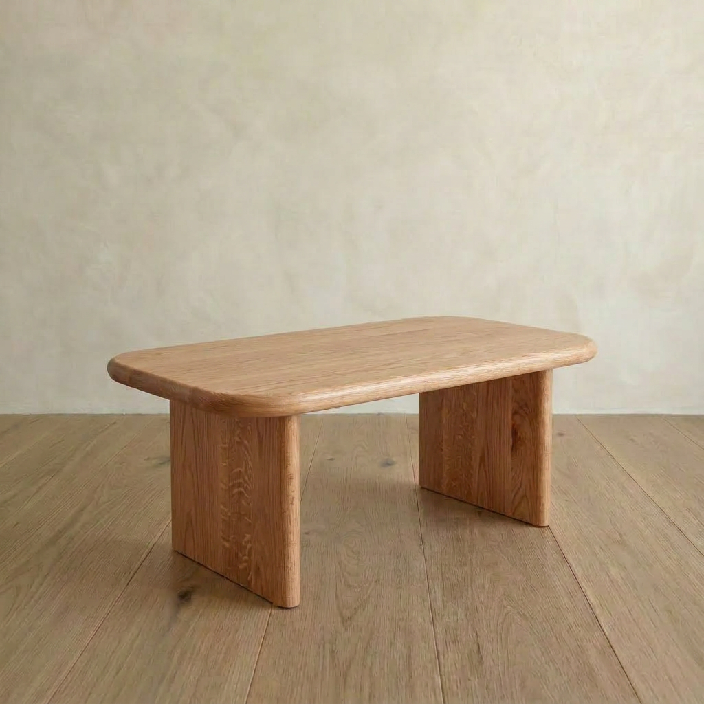 The 40 inch coffee table in red oak features a minimalist design with rounded edges and two wide, rectangular legs, placed on a light wood floor against a beige textured wall.