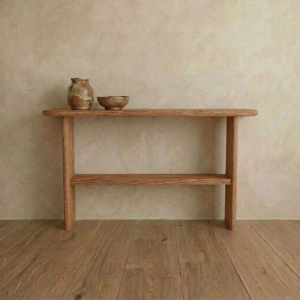 The Console table with shelf in red oak, handmade in Vancouver, stands against a beige textured wall. Two rustic ceramic vessels and a shallow bowl rest on top, while the table sits on a wooden floor.