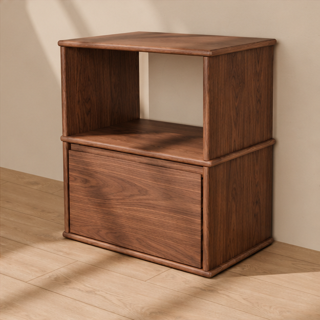 A solid wood nightstand in walnut with an open shelf above a single drawer and softly rounded edges, against a plain plaster wall.