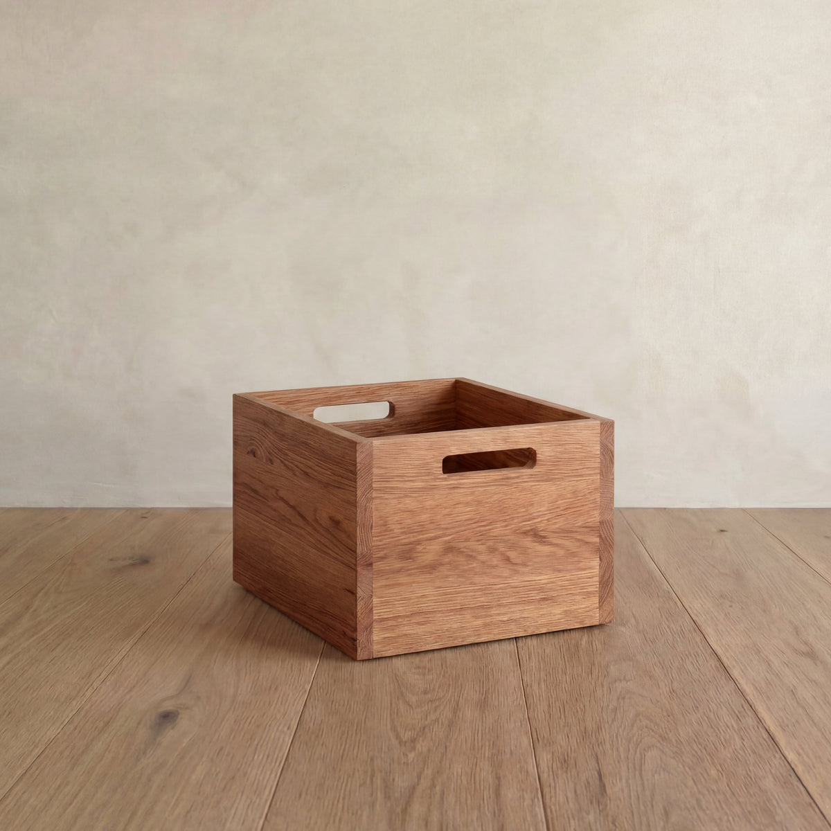 A storage cube in red oak on a wood floor, with a cutout handle on each side.