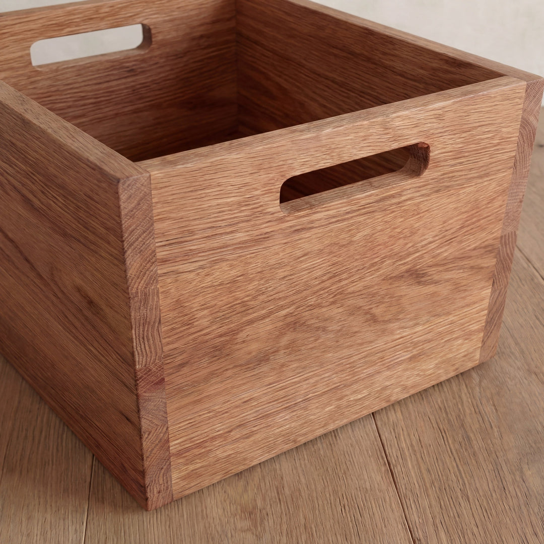 Close-up of the storage cube in red oak, showing its cutout handles and the grain of the solid wood.