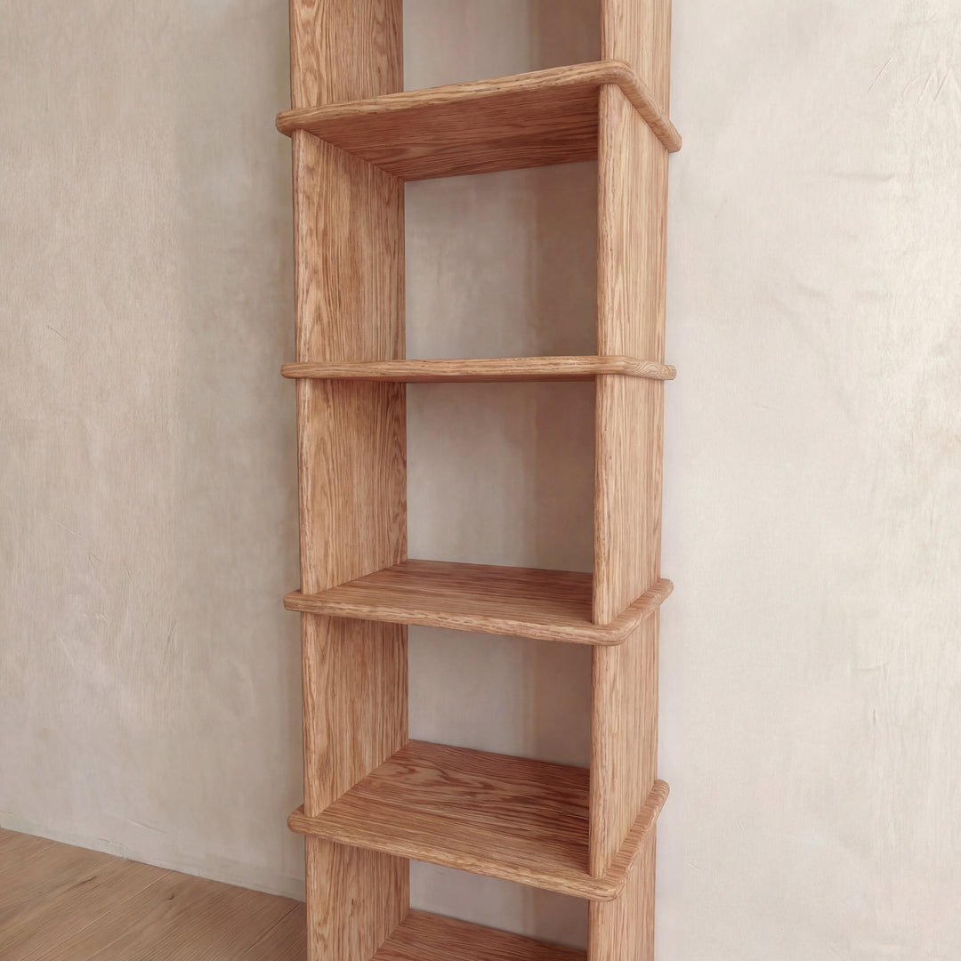 A narrow bookshelf in red oak with six empty shelves stands against a light-colored wall on a wooden floor.