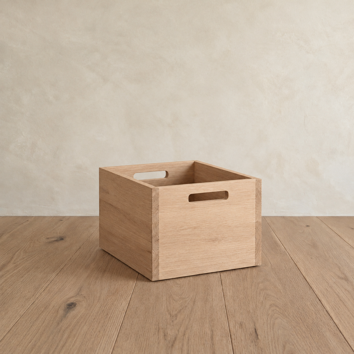 A storage cube in white oak on a wood floor, with a cutout handle on each side.