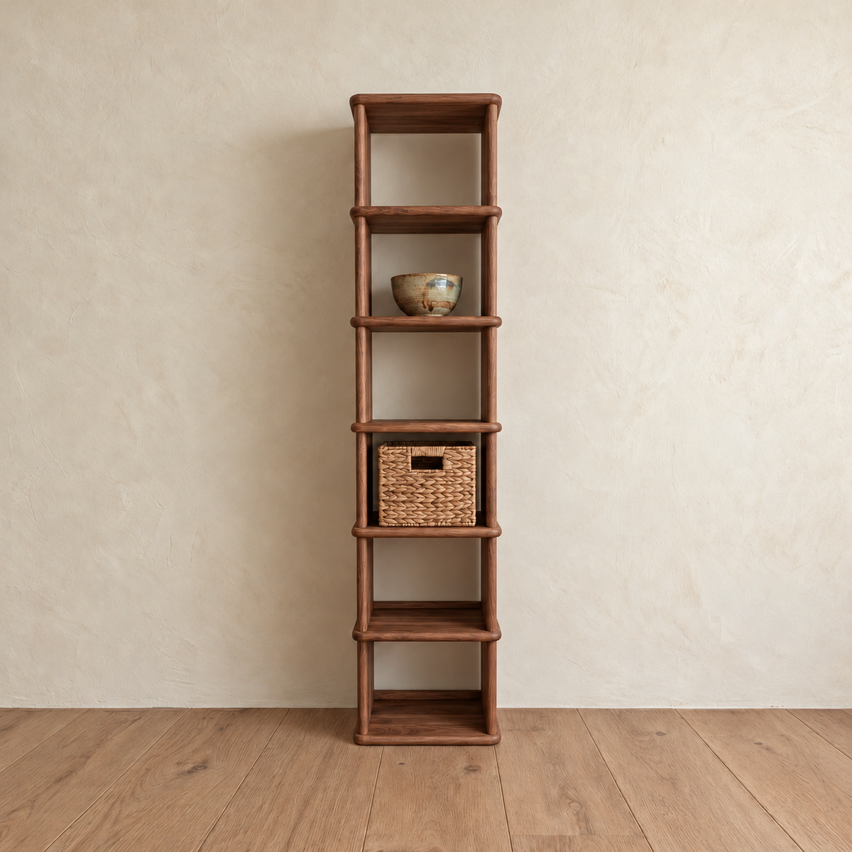 The tall narrow bookcase in walnut against a plaster wall, with a ceramic bowl and a woven basket on its shelves.