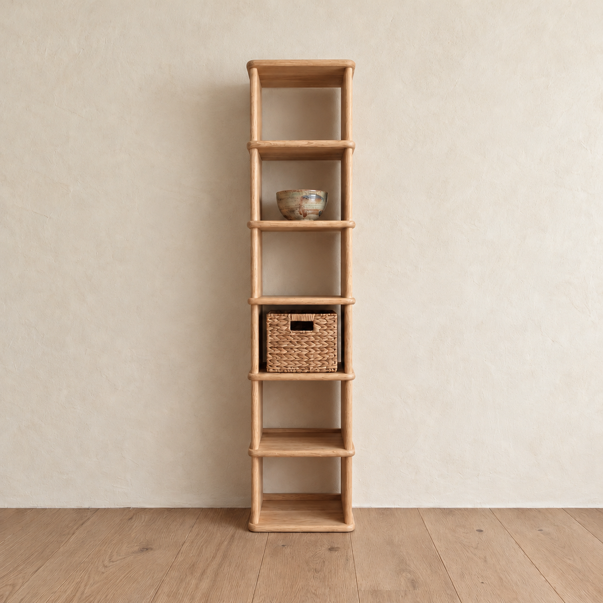 The tall narrow bookcase in white oak against a plaster wall, with a ceramic bowl and a woven basket on its shelves.