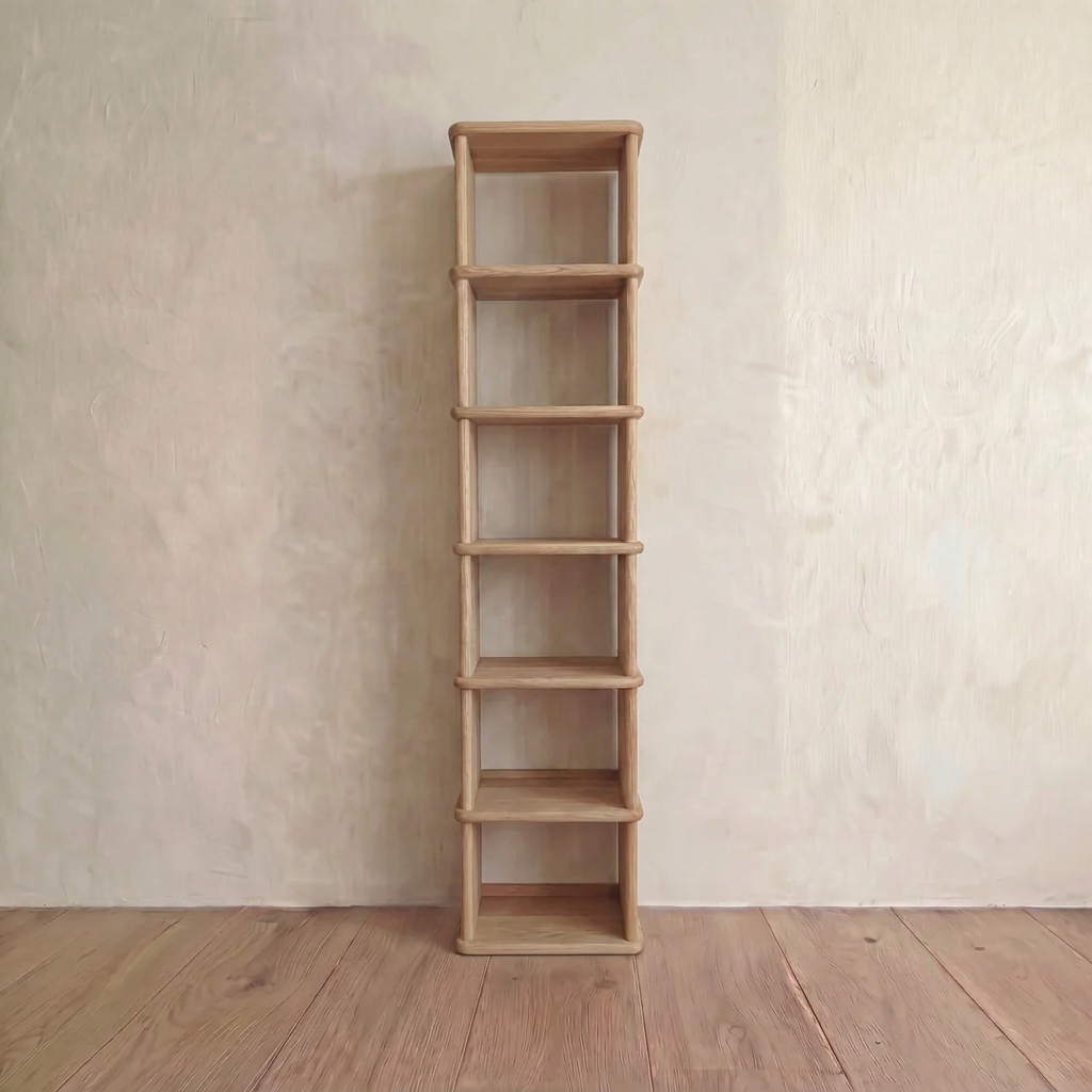 The tall narrow bookcase in white oak, handmade in Vancouver, features six sleek shelves and a minimalist design, standing against a light wall on a wooden floor for versatile styling.