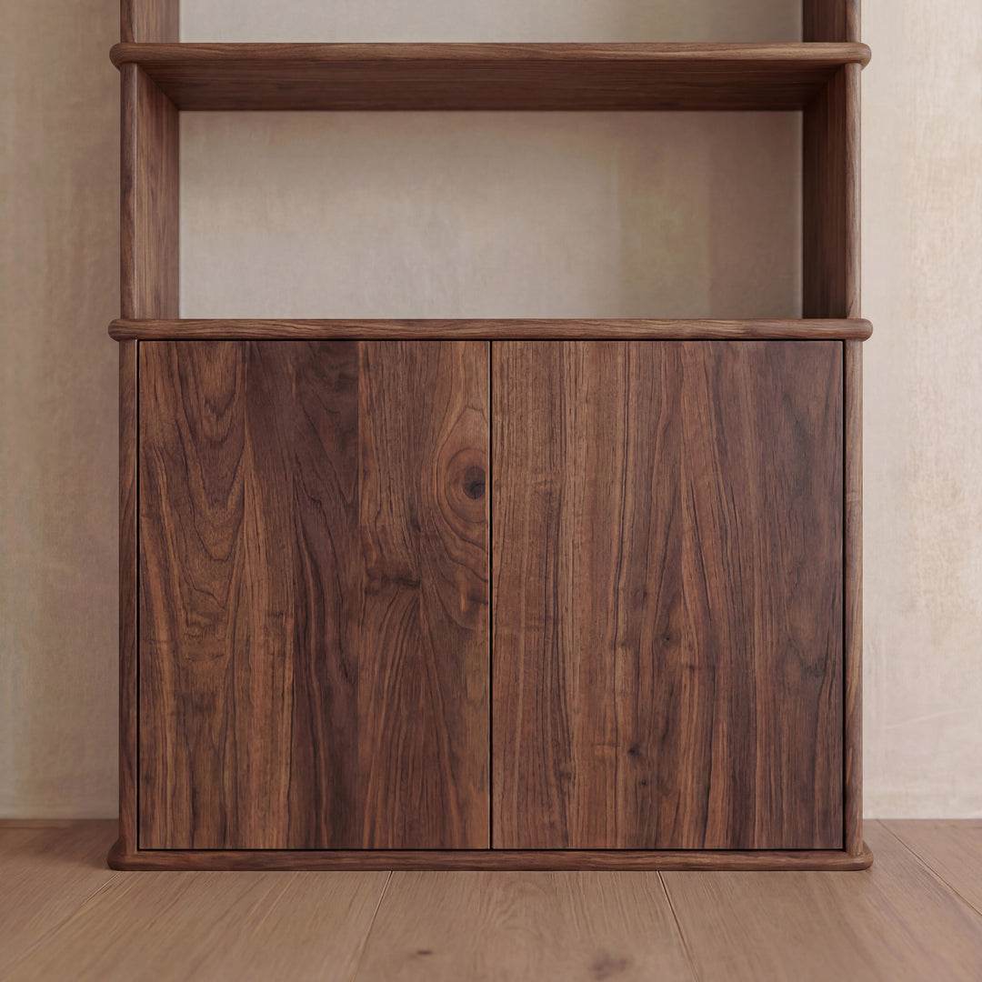A close-up view of the lower section of the Cabinet bookshelf in walnut features two closed, push-to-open doors that highlight the natural wood grain. The unit is positioned on a light wooden floor against a beige wall.