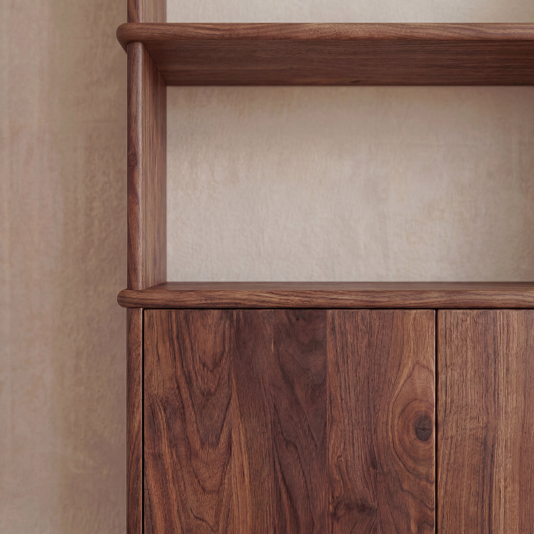 A close-up of the Cabinet bookshelf in walnut, featuring a natural wood grain finish and push-to-open doors, set against a beige wall.