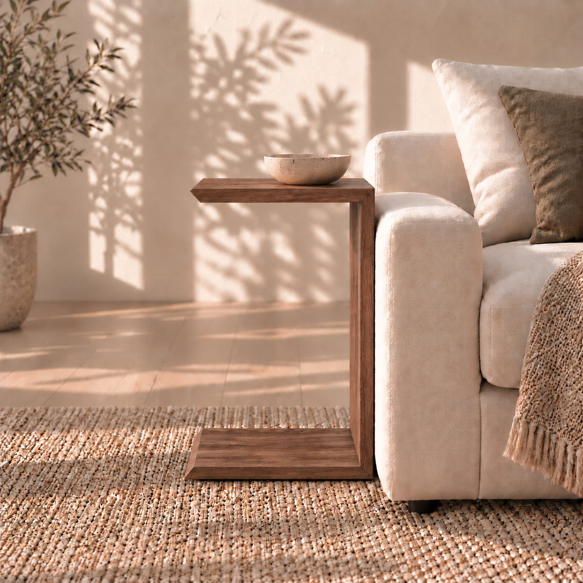 A handmade C-shaped solid walnut Sofa side table in walnut holds a small bowl next to an upholstered sofa.