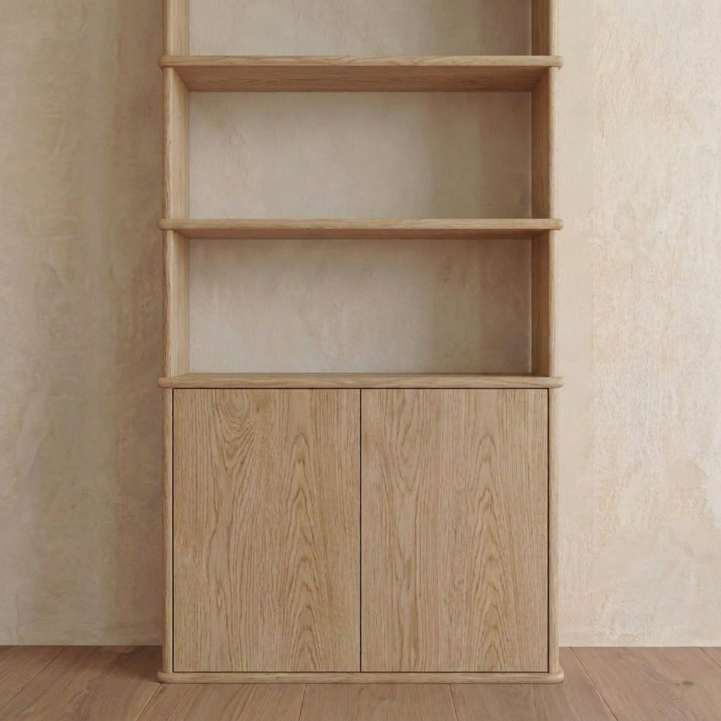 The Cabinet bookshelf in white oak features three open shelves above a two-door cabinet, set against a beige textured wall on a wooden floor. Handmade and inspired by Vancouver furniture design, this piece combines style and functionality to provide a versatile storage solution for any space.