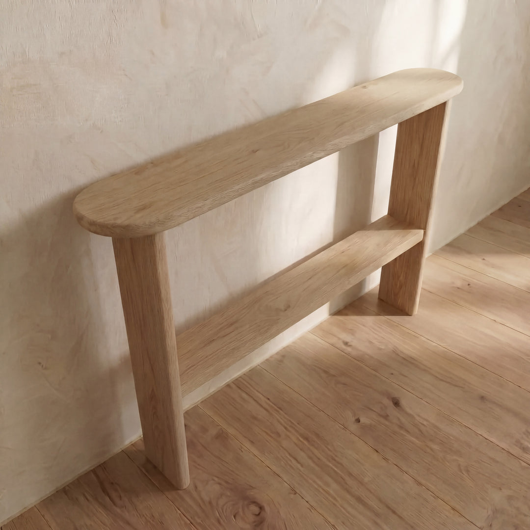 The Console table with shelf in white oak features a minimalist handmade design with rounded edges and a single lower shelf, shown against a light-colored textured wall on a wooden floor.