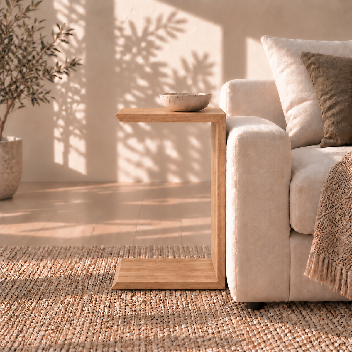 Handmade C-shaped Sofa side table in white oak holding a small bowl next to a sofa.