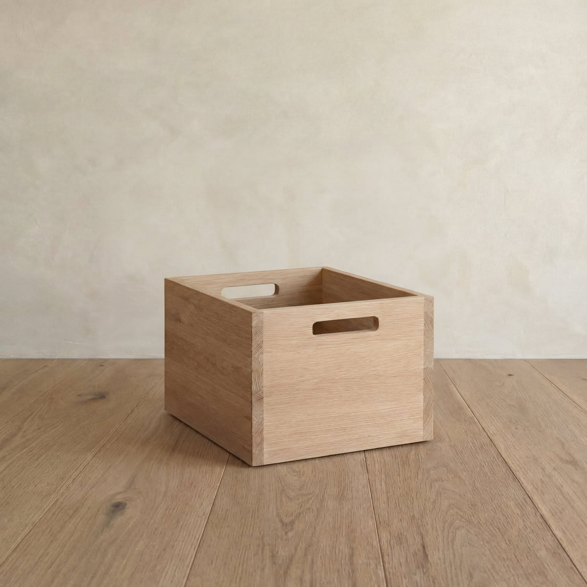 A storage cube in white oak on a wood floor, with a cutout handle on each side.